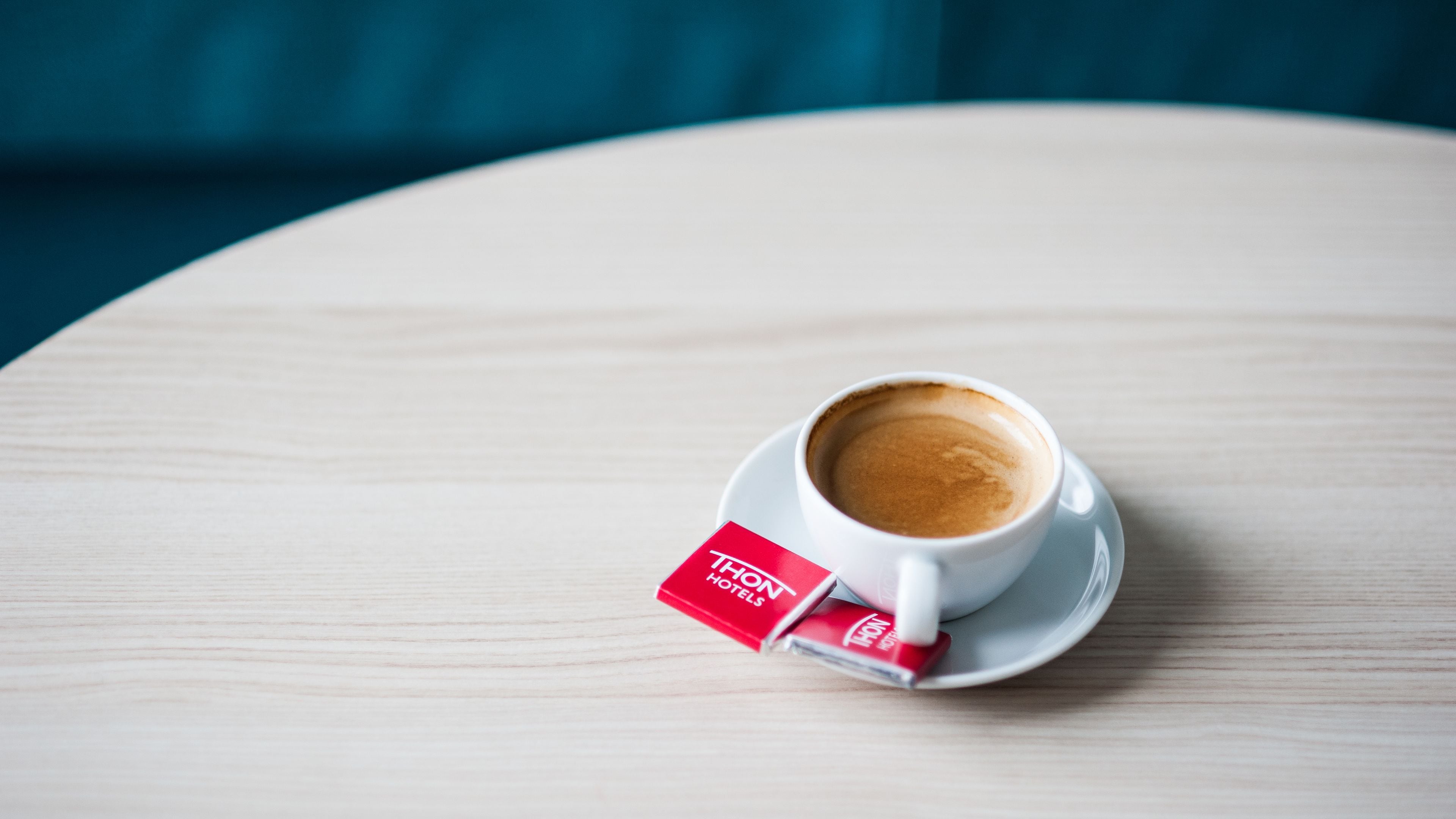 A cup of coffee on a white saucer with a red label on a round wooden table.