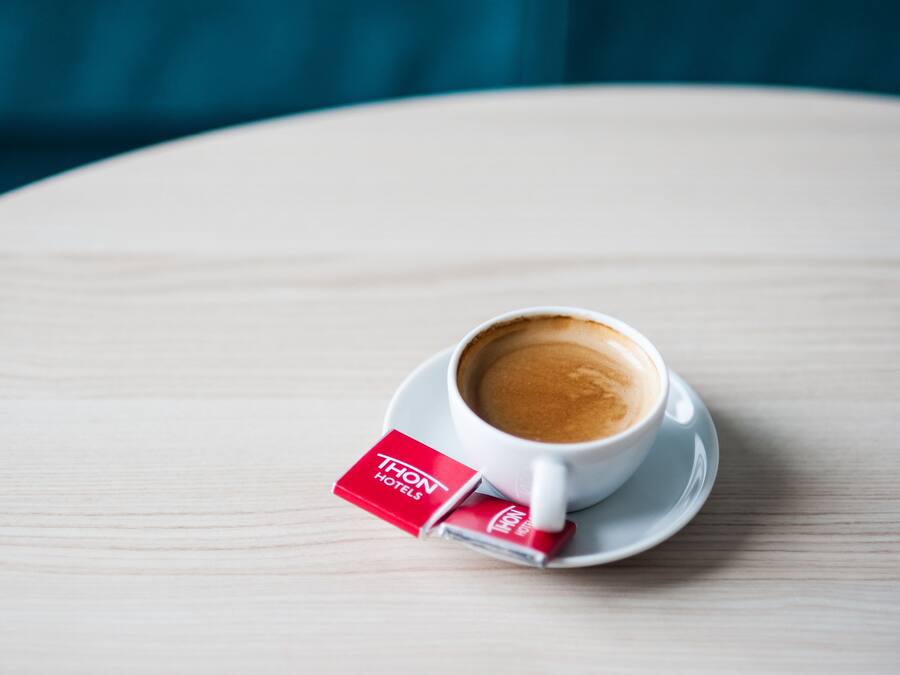 A cup of coffee on a white saucer with a red label on a round wooden table.