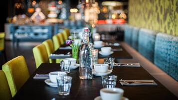 A restaurant table set with a bottle, glasses, and plates, with a blue upholstered bench and yellow chairs in the background.