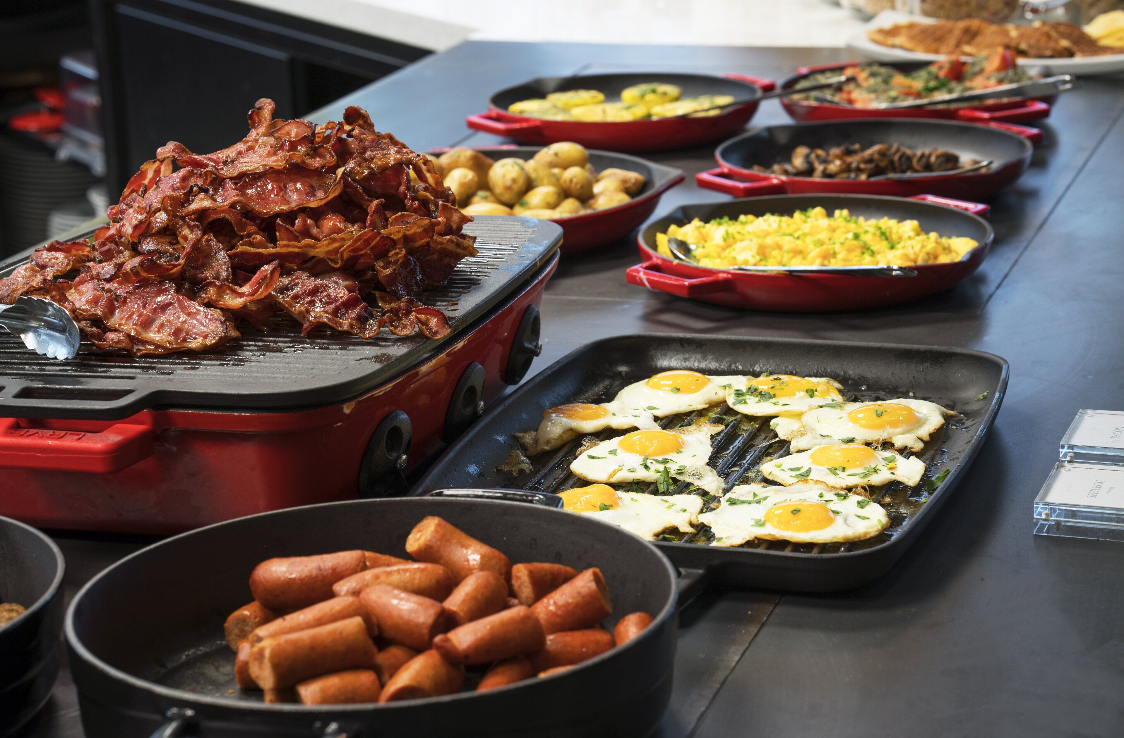 A buffet with various dishes including bacon, sausages, eggs, and potatoes.