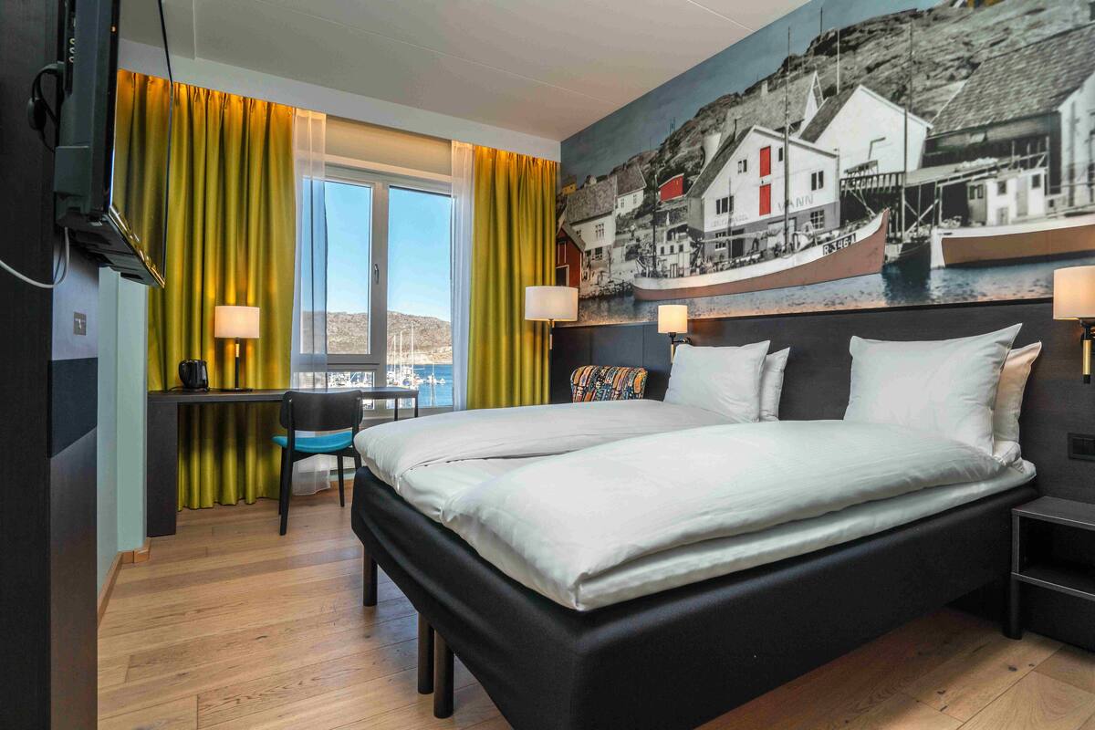 A hotel room with a bed, desk, chair, and a large window with curtains.