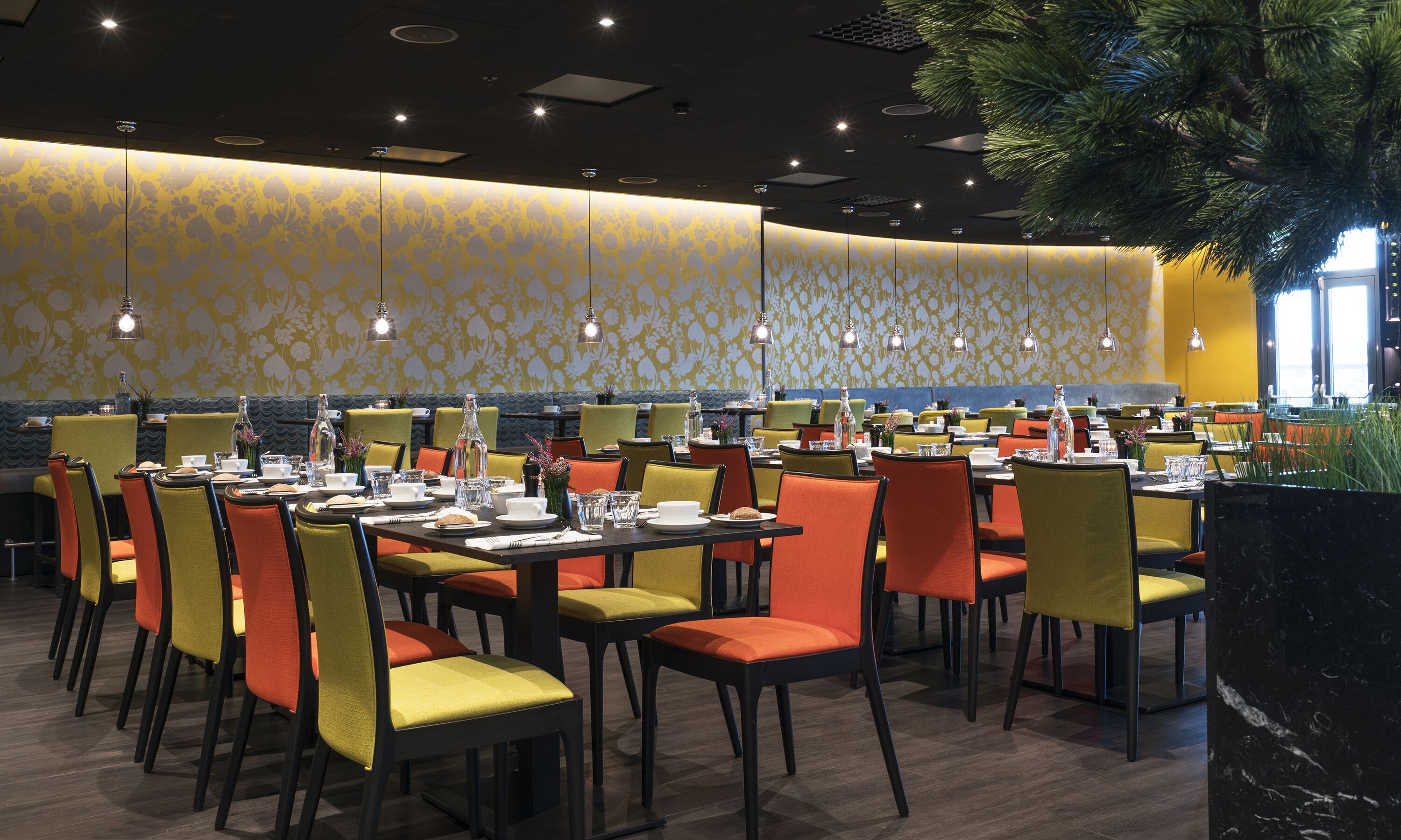Un restaurante con varias mesas y sillas, un papel tapiz decorativo y lámparas colgantes.