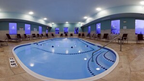 Une grande piscine intérieure avec des bords carrelés, entourée de chaises longues et de tables.