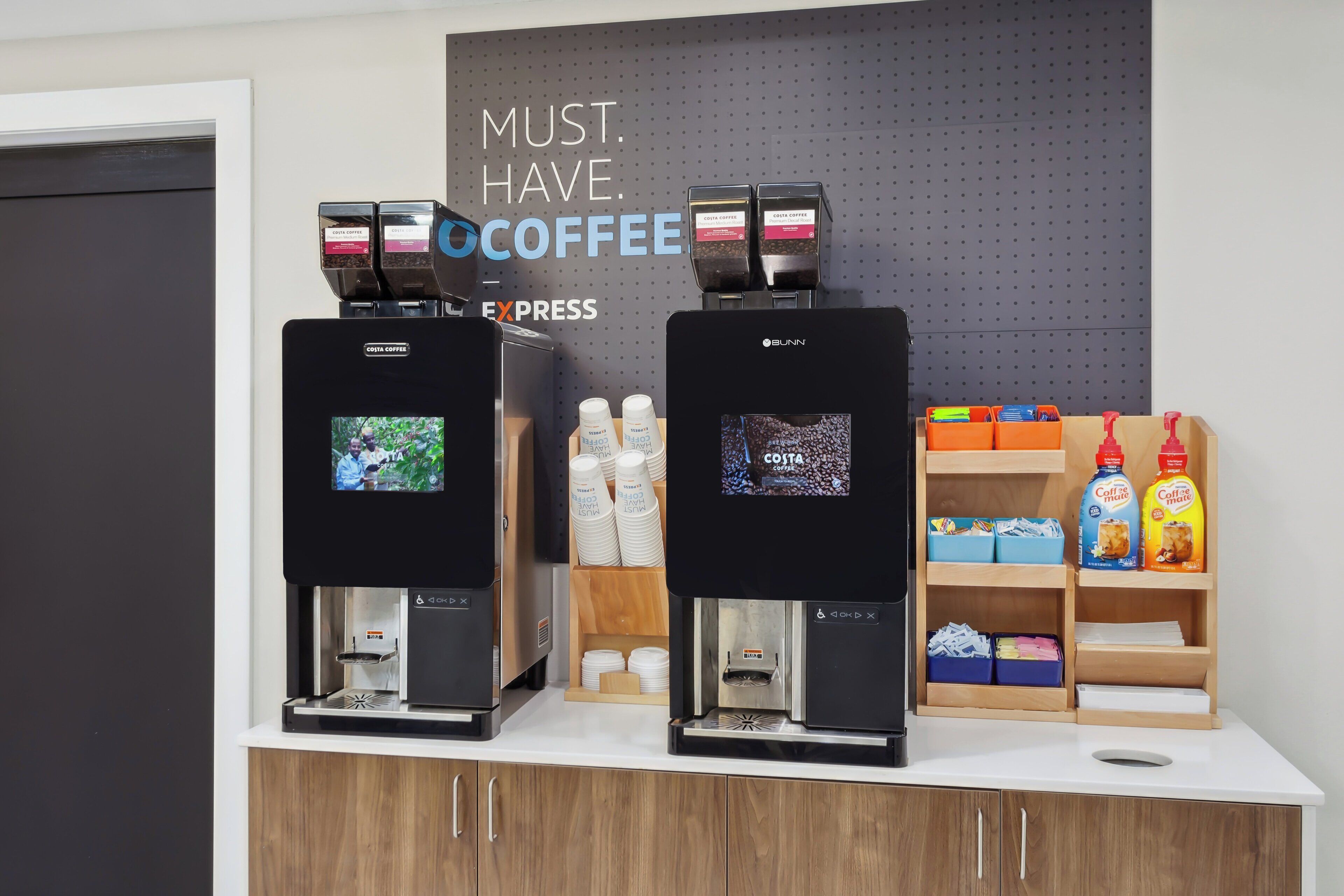 Two coffee machines with digital displays, a coffee station with disposable cups, and a shelf with coffee products.
