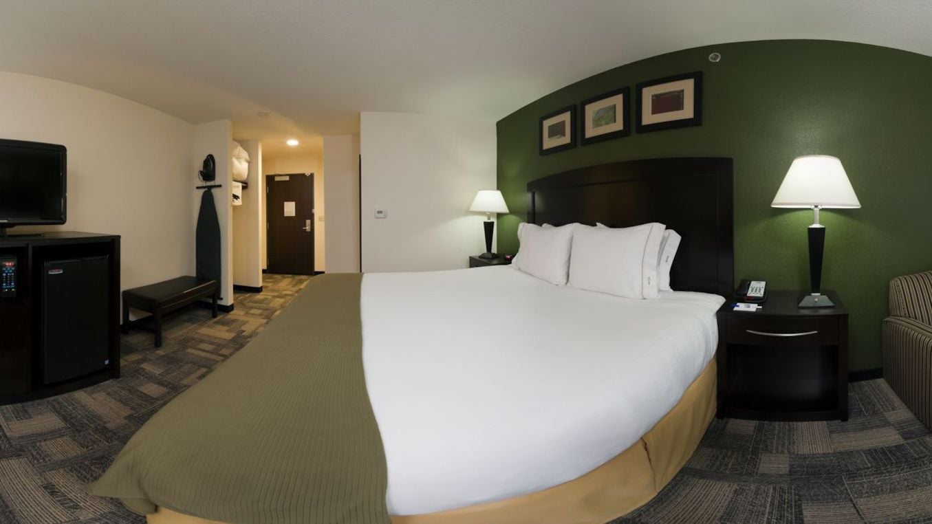 A hotel room with a large bed, a television, a desk with a computer, and a chair.
