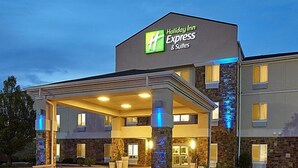 Un bâtiment de l’hôtel Holiday Inn Express & Suites doté d’une entrée couverte, d’une façade en pierre et d’une enseigne lumineuse.