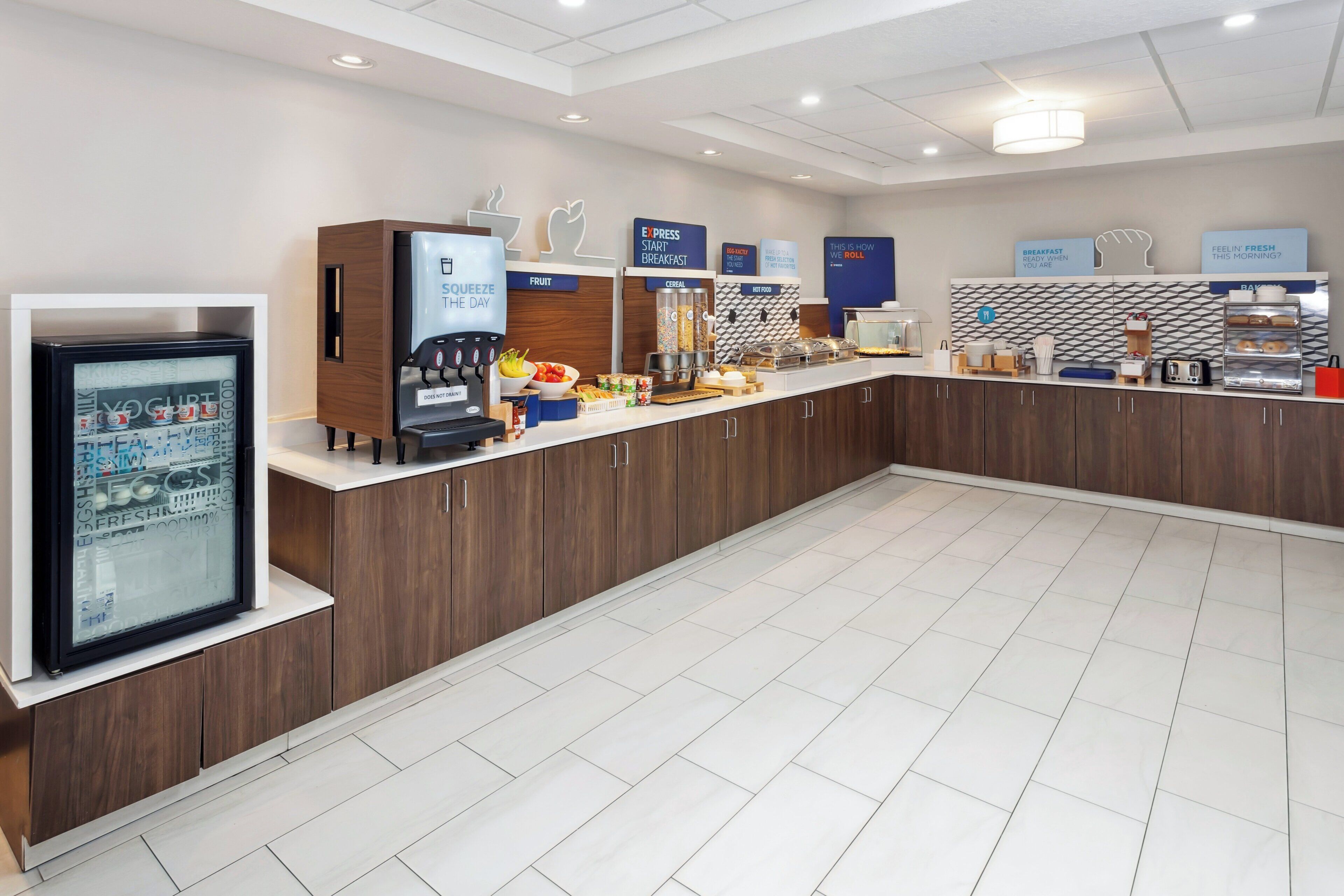 Un espace moderne dédié au petit-déjeuner, avec un buffet où les clients peuvent se servir eux-mêmes, proposant notamment des fruits, des céréales et des boissons chaudes.