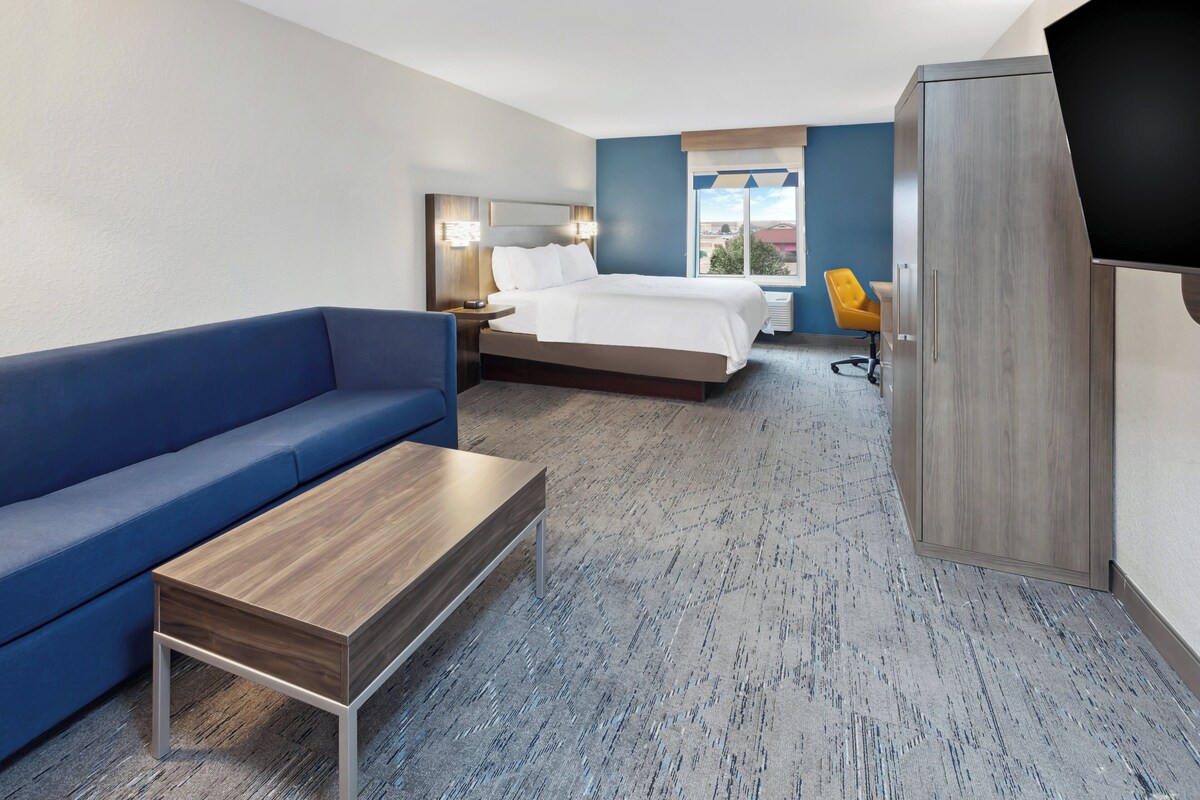 A hotel room with a bed, a blue sofa, a wooden coffee table, a TV, and a wardrobe.