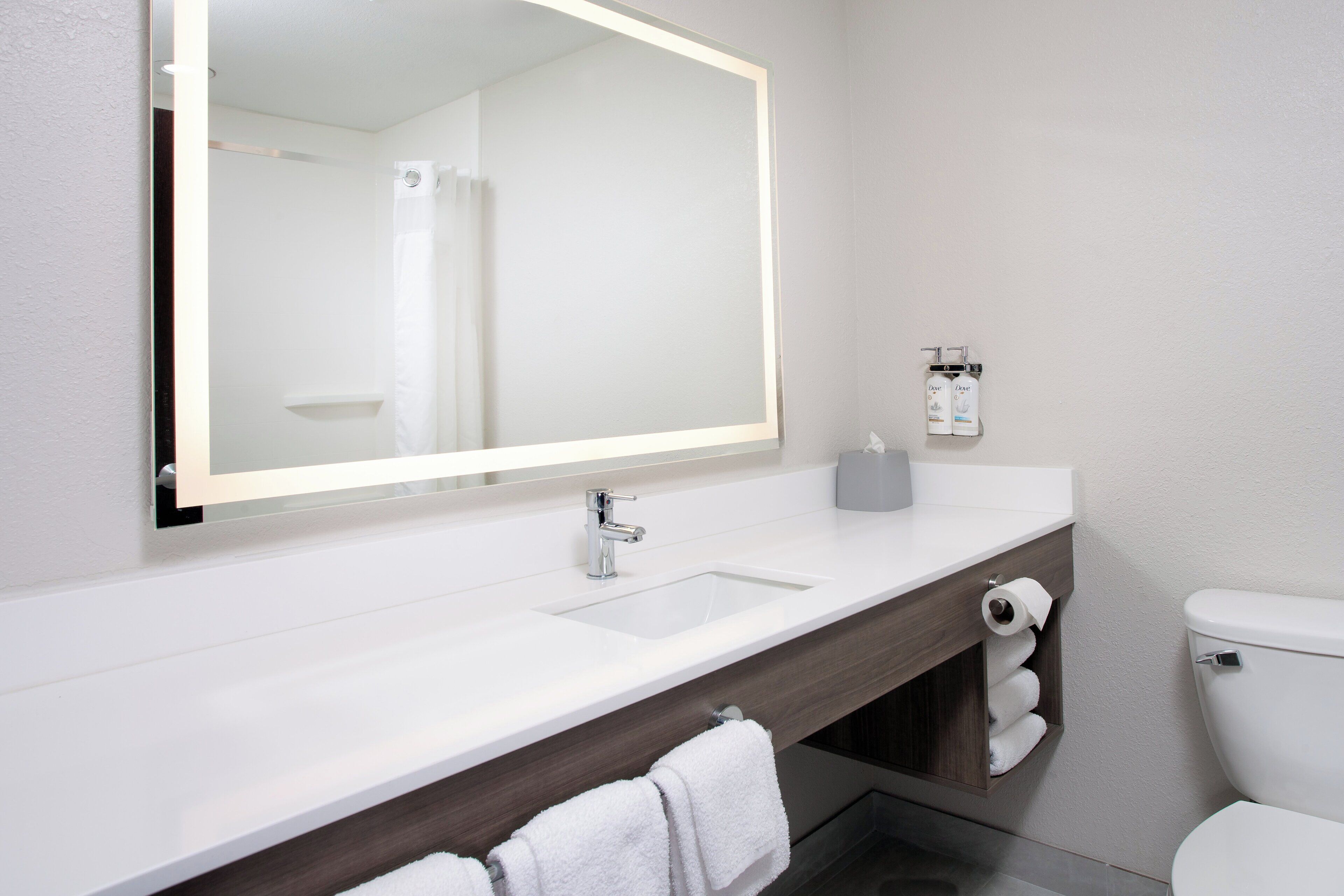A modern bathroom with a large mirror, white sink, and toilet.