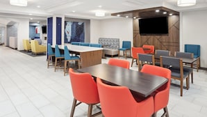 A modern conference room with a large table and multiple chairs, a TV mounted on the wall, and a seating area with sofas and chairs. - Holiday Inn Express & Suites Pekin (Peoria Area) by IHG (Pekin)
