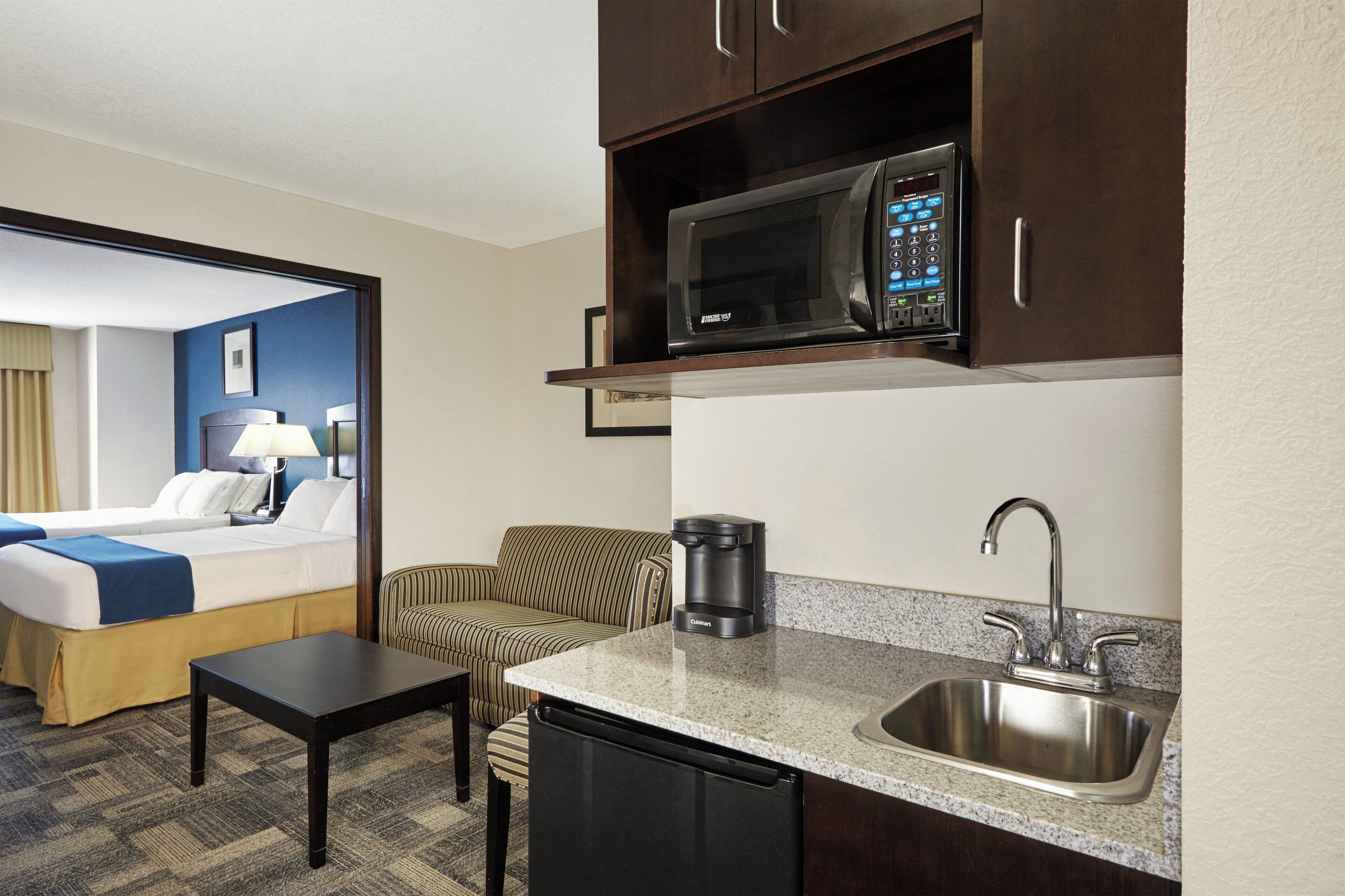 A compact hotel room with a kitchenette, including a microwave, coffee maker, sink, and a small dining table.