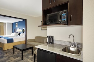 Habitación de hotel compacta con kitchenette, que incluye microondas, cafetera, lavamanos y una pequeña mesa de comedor.