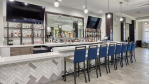 A bar area with a herringbone tile backsplash, a flat-screen TV, and a variety of liquor bottles.