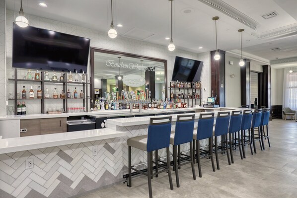 A bar area with a herringbone tile backsplash, a flat-screen TV, and a variety of liquor bottles. - Holiday Inn Hotel & Suites Madison West - Middleton by IHG (Madison)