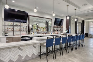 A bar area with a herringbone tile backsplash, a flat-screen TV, and a variety of liquor bottles.