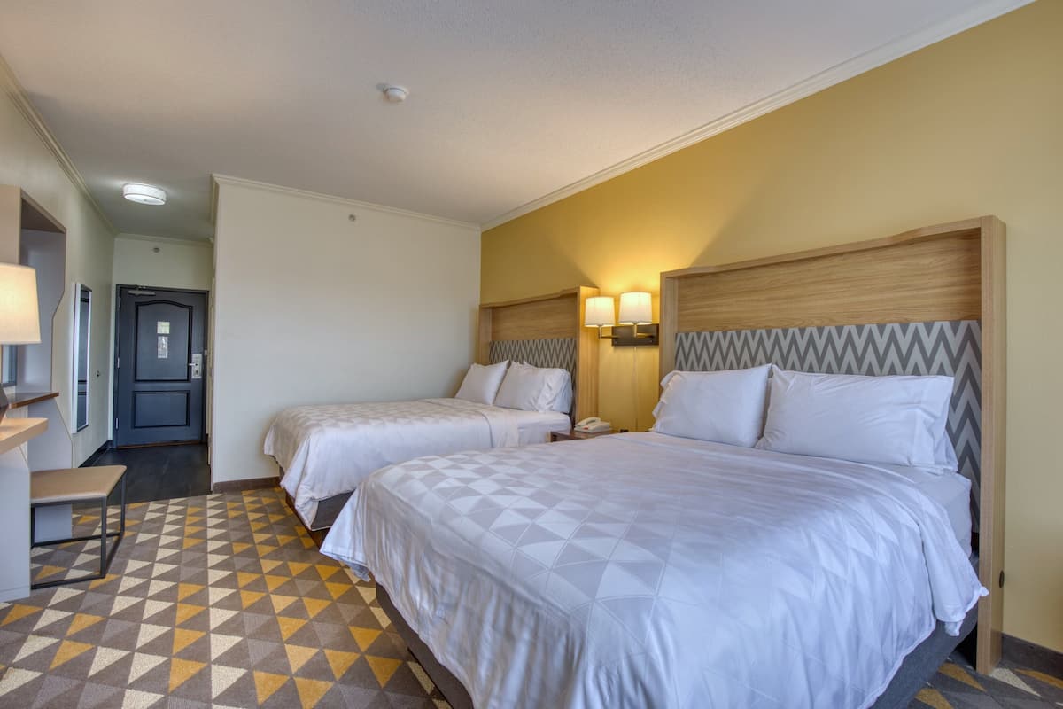 A hotel room with two beds, a desk, and a chair. There is a door leading to another room.