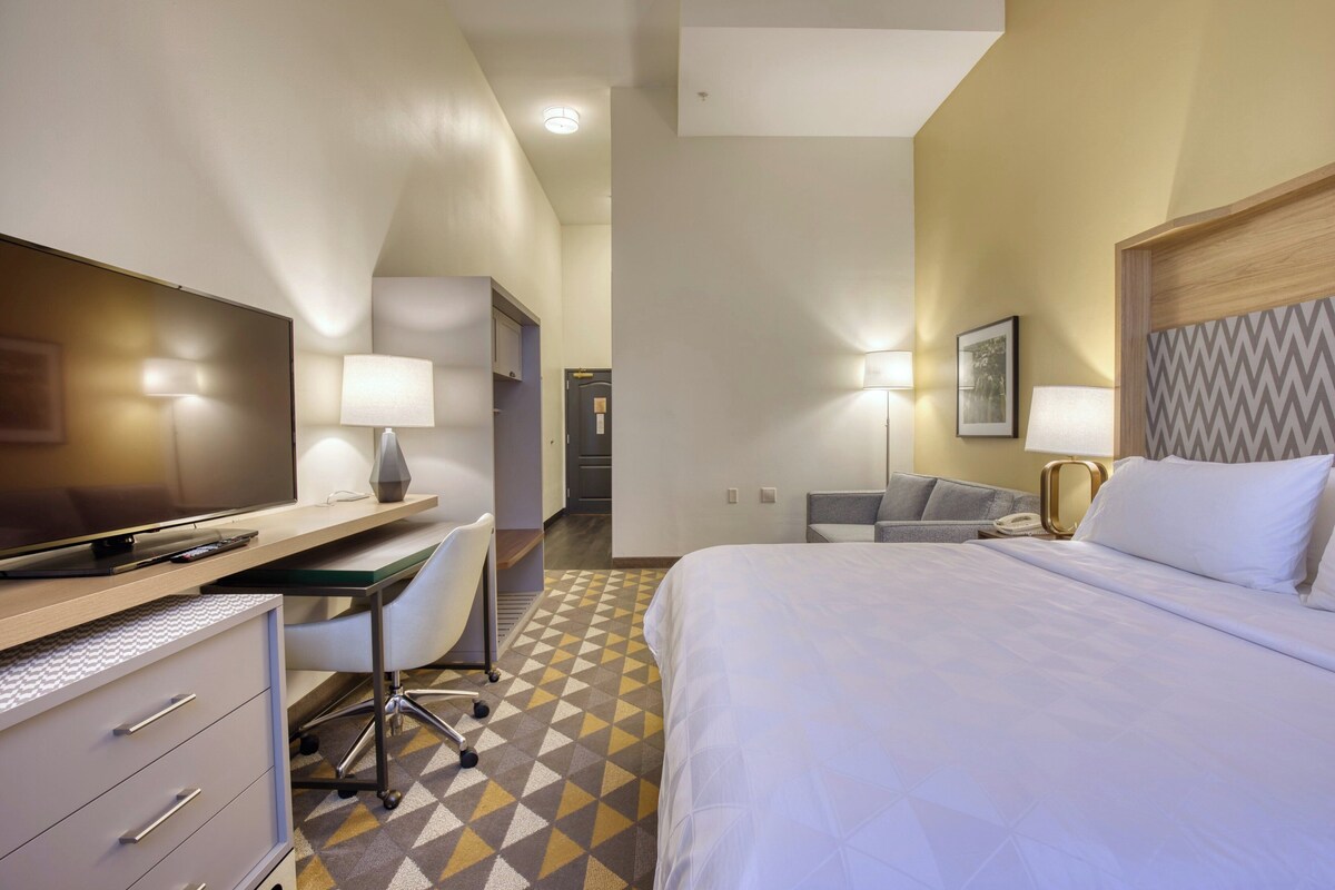 A hotel room with a bed, desk, chair, television, and lamps.