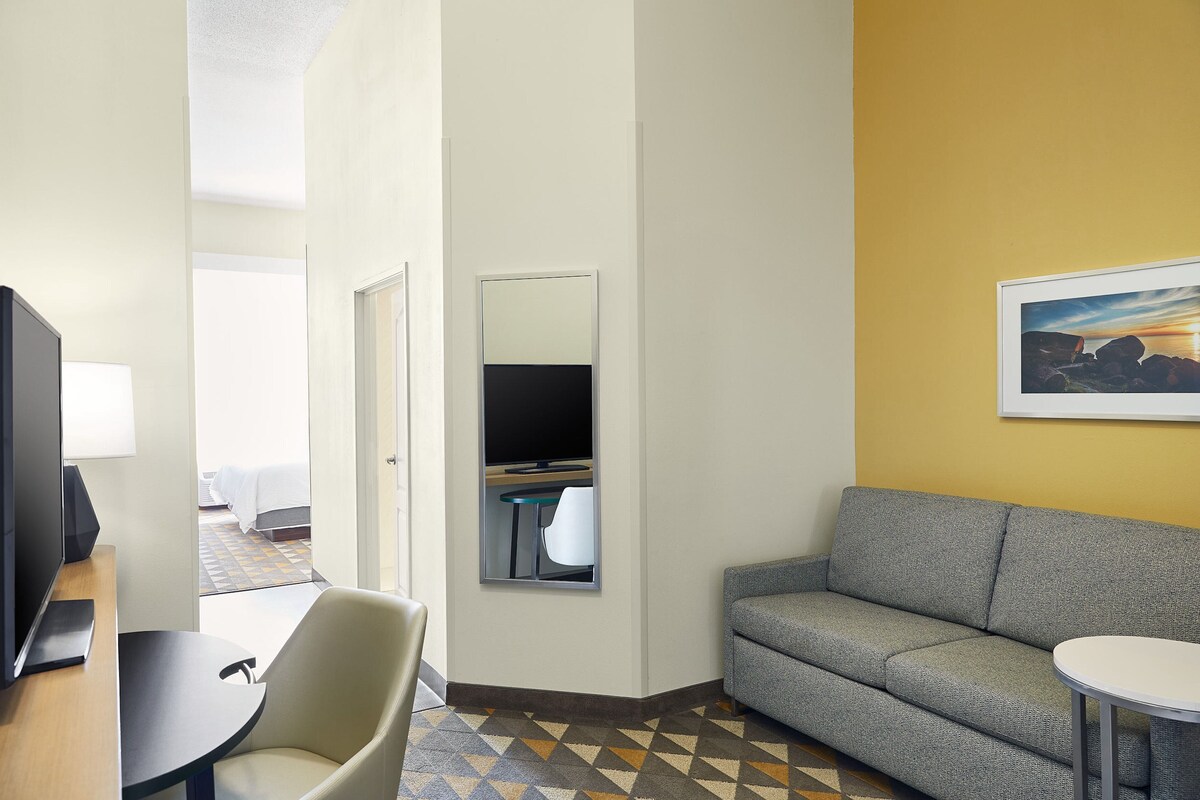 A hotel room with a sofa, a small table, a TV, and a framed picture on the wall.