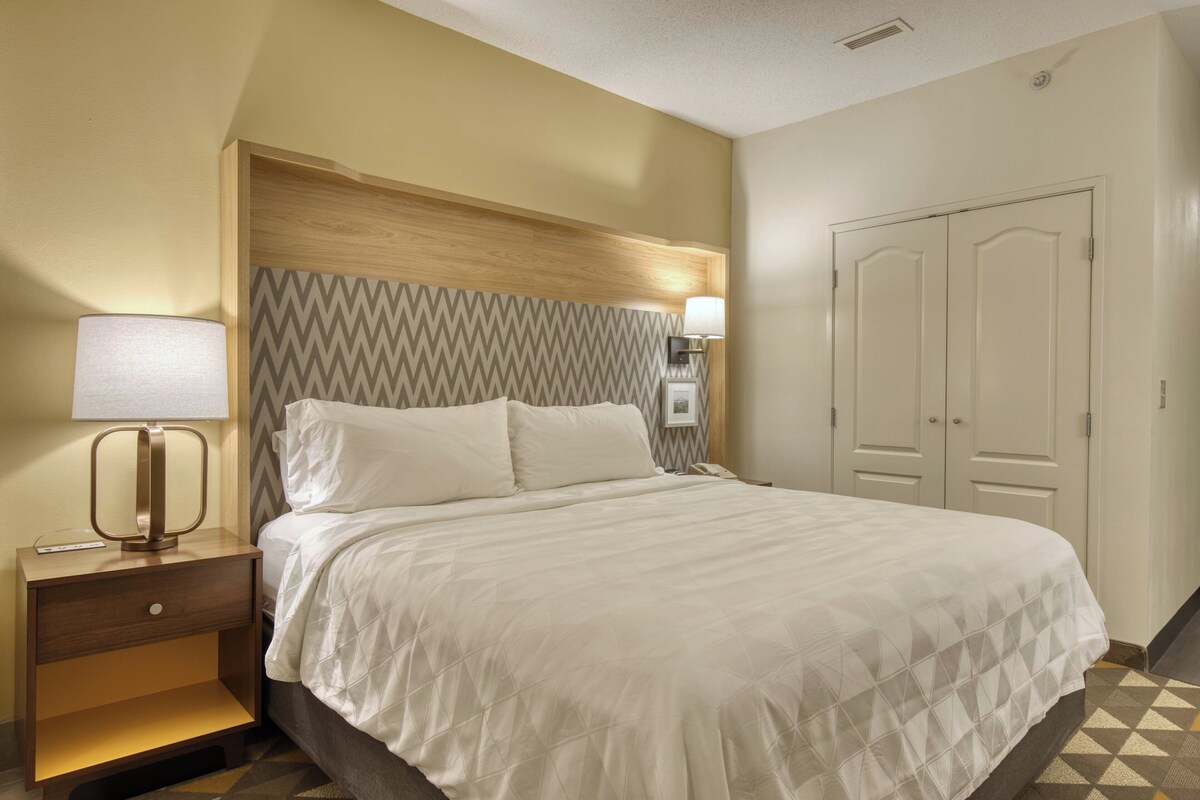 A hotel room with a bed, nightstand, lamp, and wardrobe.