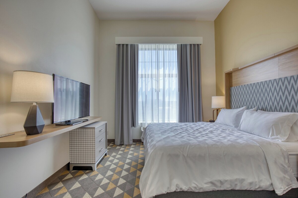 A hotel room with a bed, a desk with a TV, a lamp, and a patterned floor.