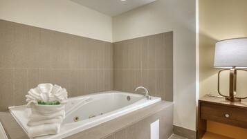 A modern bathroom with a large bathtub, a towel rack with towels, and a bedside table with a lamp.