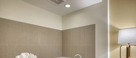 A modern bathroom with a large bathtub, a towel rack with towels, and a bedside table with a lamp.