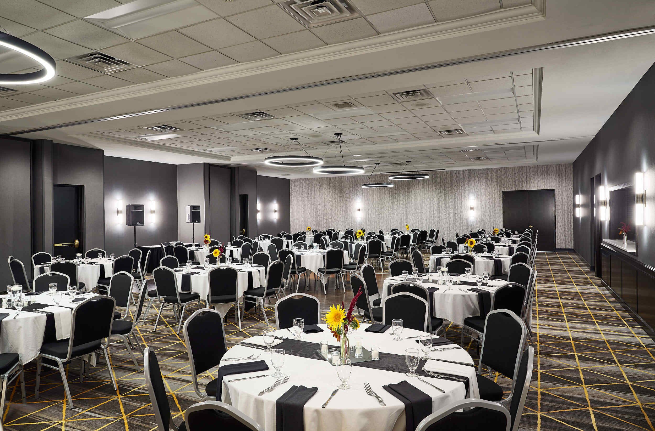 A banquet hall with round tables, black chairs, and white tablecloths.