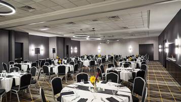 A banquet hall with round tables, black chairs, and white tablecloths.