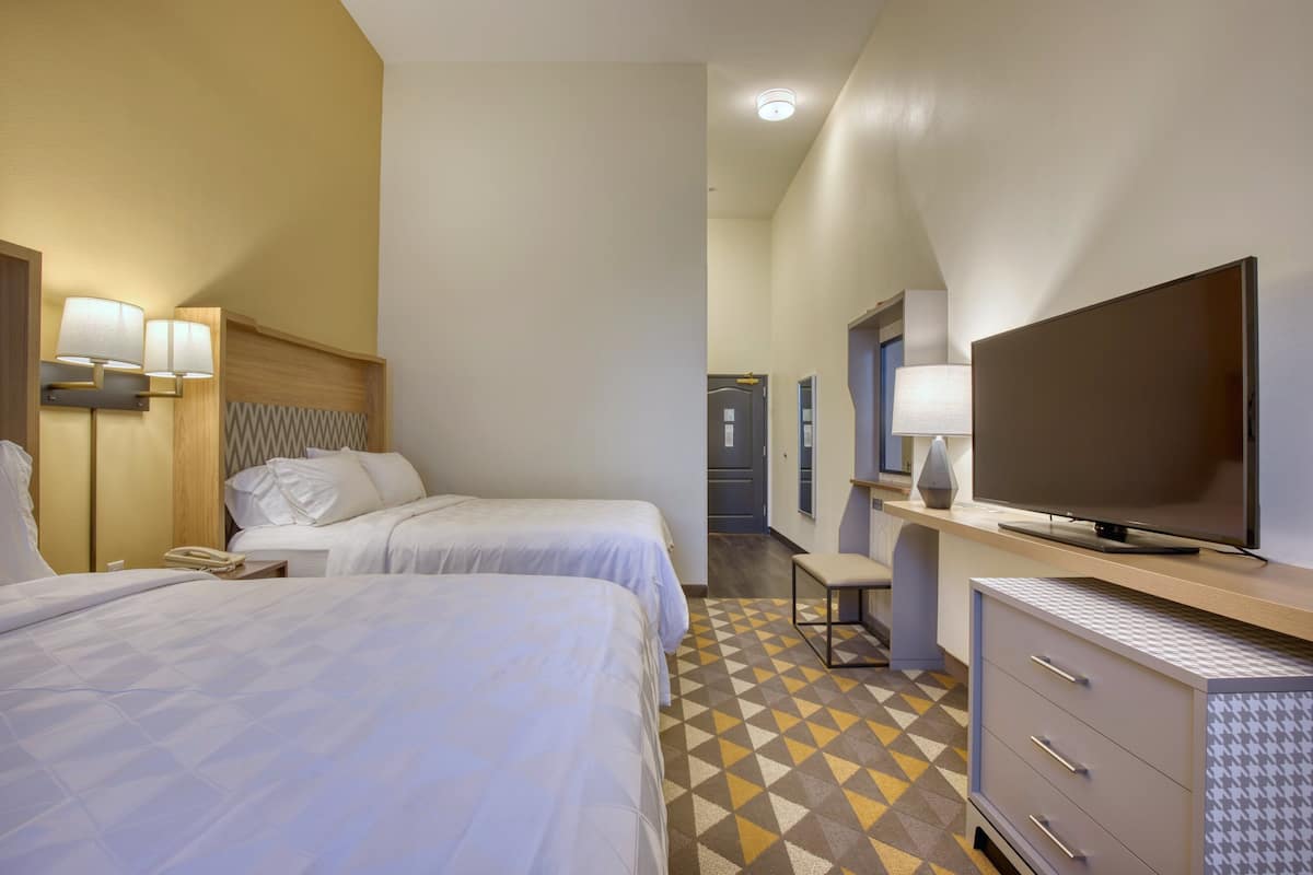 A hotel room with two beds, a TV, a desk, and a bathroom in the background.