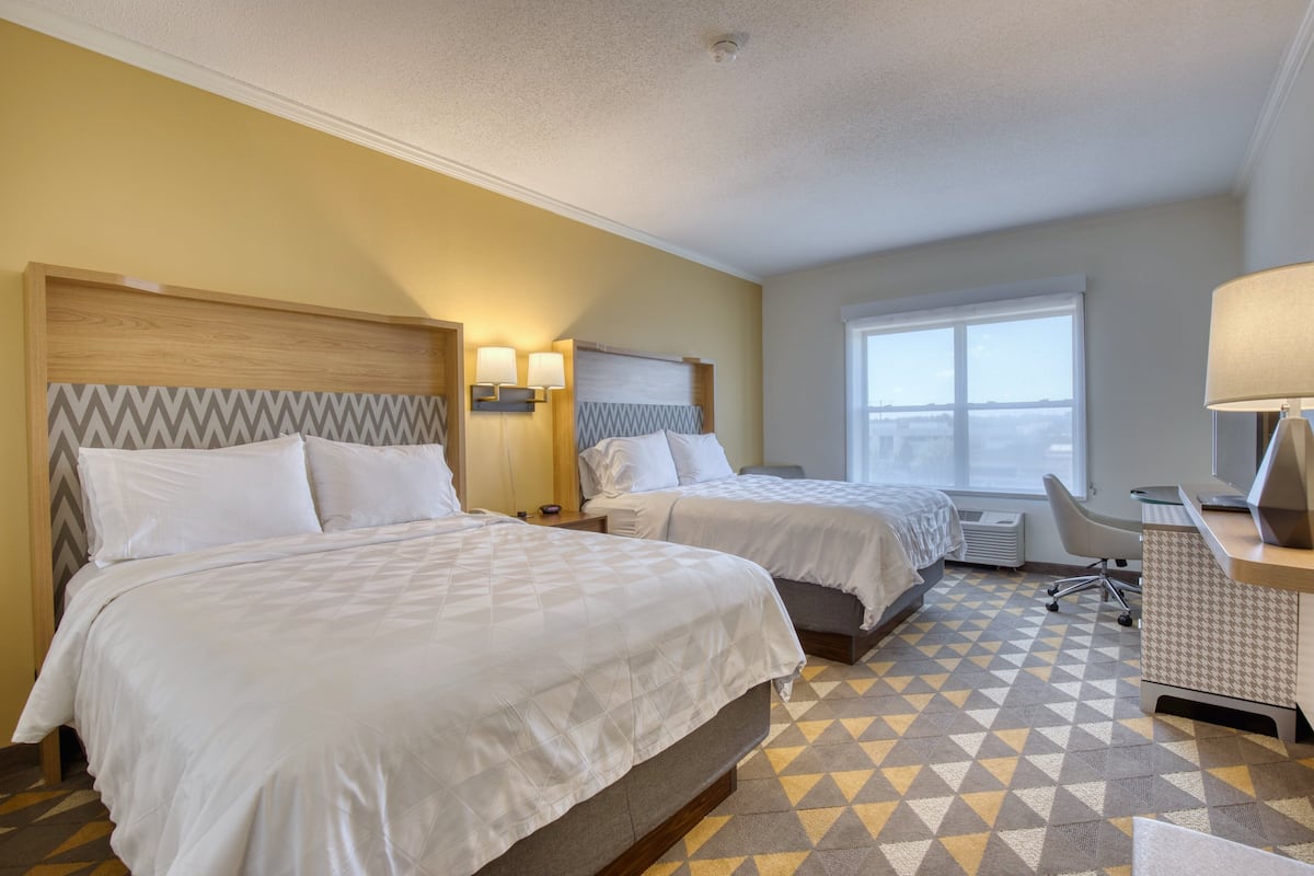 A hotel room with two beds, a desk, and a chair.