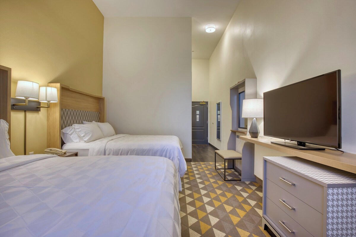 A hotel room with two beds, a television, a desk, and a chair.