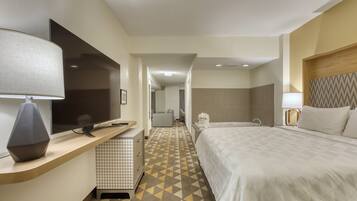 A hotel room with a bed, a desk with a lamp, a television, and a bathroom with a shower.