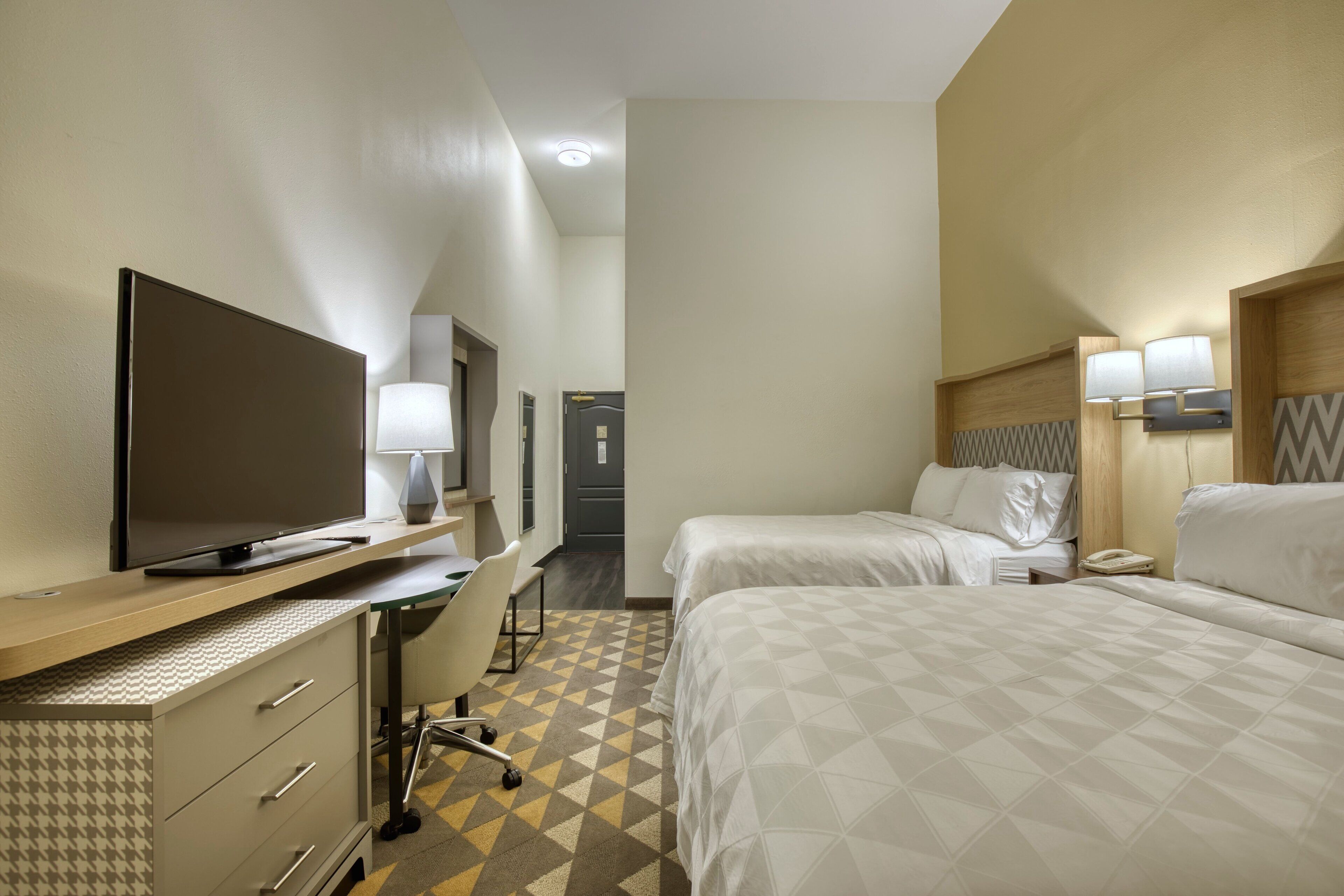 A hotel room with a bed, a desk with a TV, a chair, and a lamp.