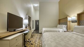 A hotel room with a bed, a desk with a TV, a chair, and a lamp.