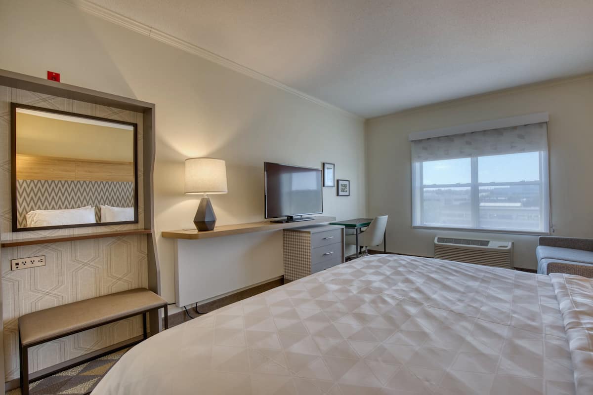 A hotel room with a large bed, a desk with a chair, a TV, a mirror, and a window with a view.