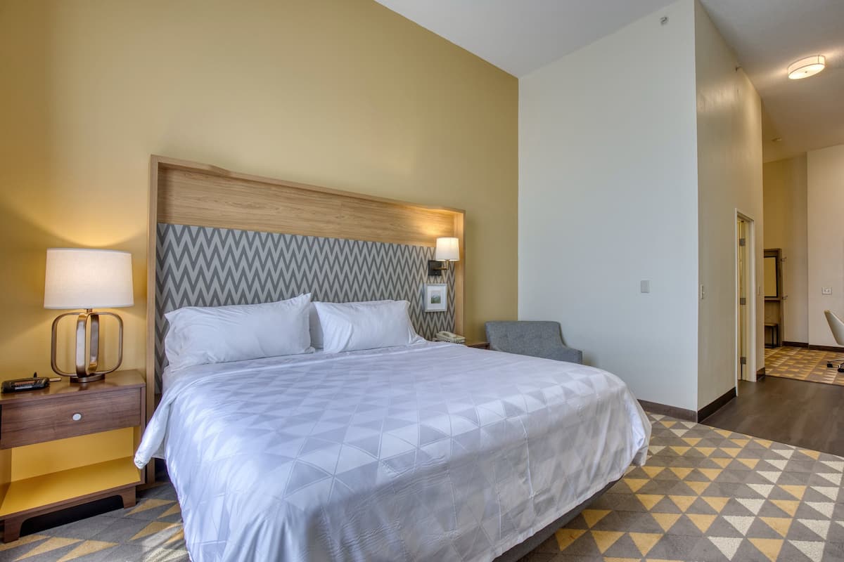 A hotel room with a large bed, a bedside table with a lamp, and a chair.