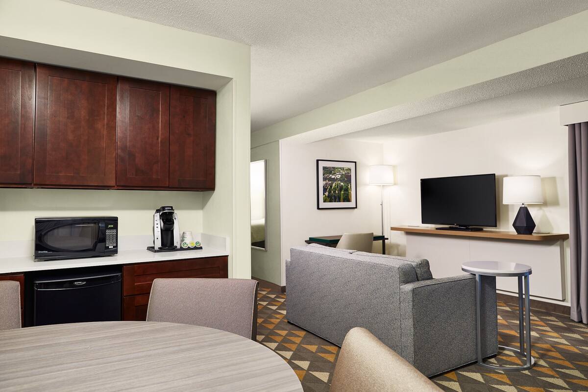 A hotel room with a kitchenette, a sofa, a TV, and a small table.