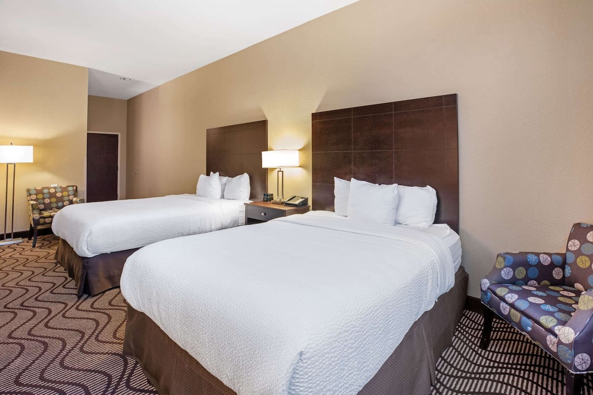 Een hotelkamer met twee bedden, een stoel en een lamp.