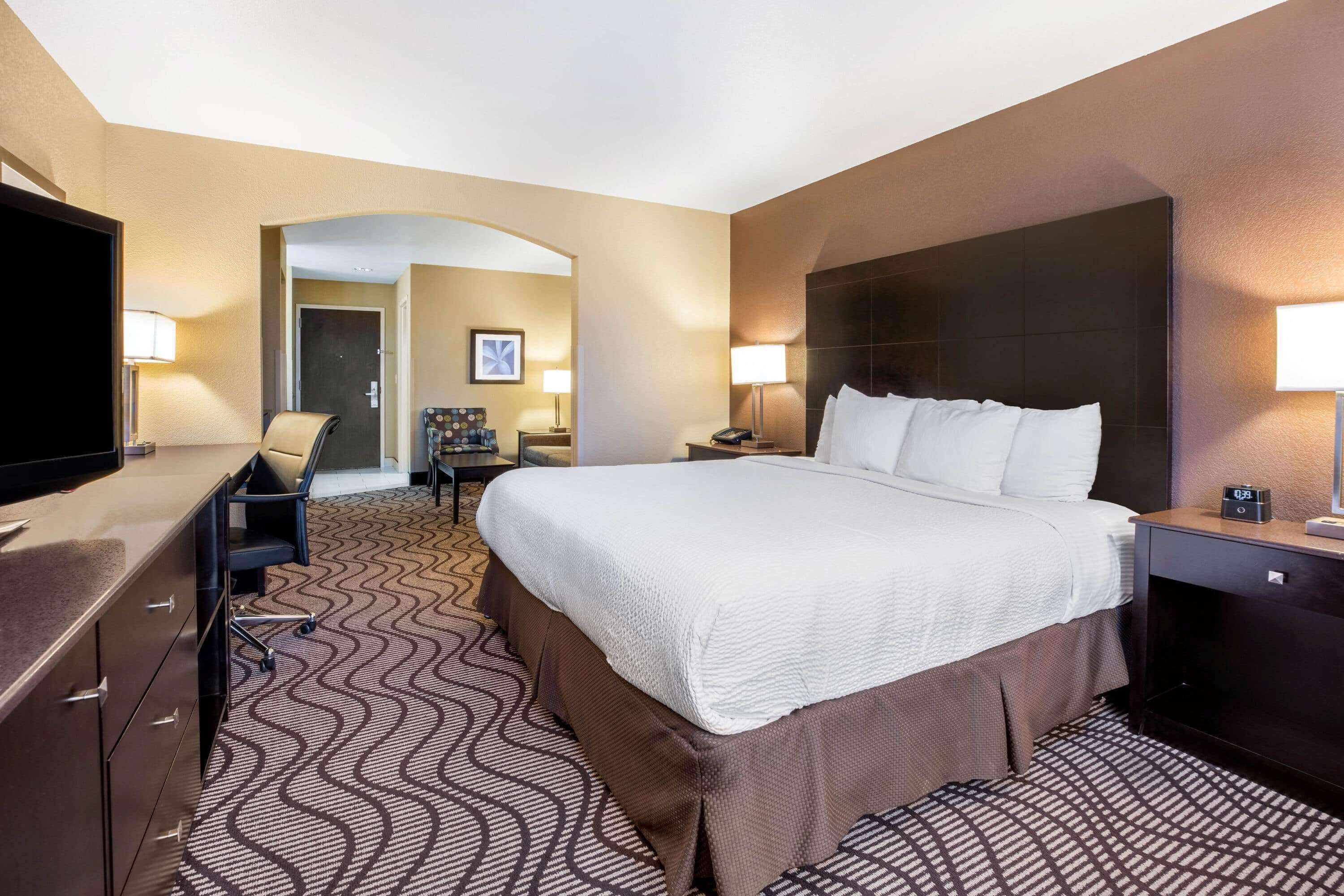 A hotel room with a large bed, a desk with a chair, a TV, and a desk lamp.
