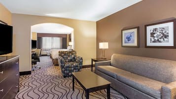 A hotel room with a sofa, armchair, TV, and a patterned carpet.