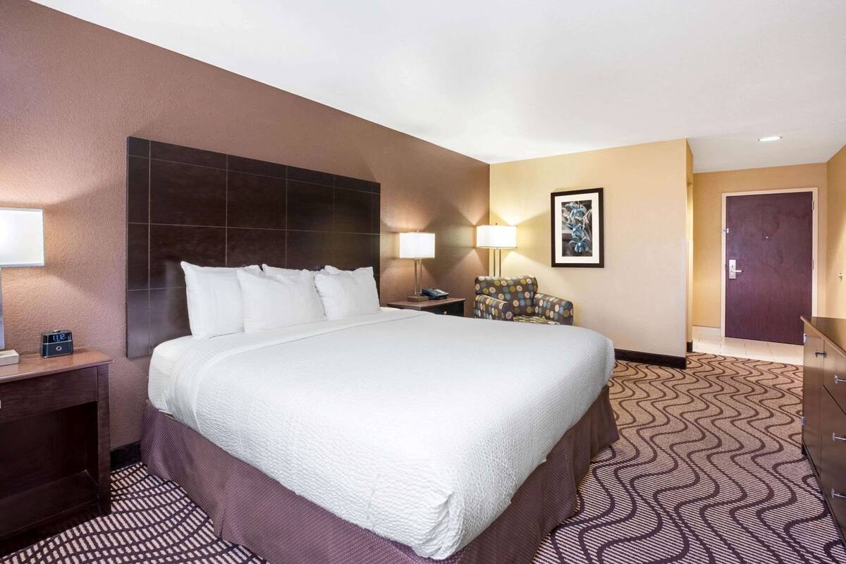 Een hotelkamer met een groot bed, nachtkastjes, een stoel, een bureau en een deur.
