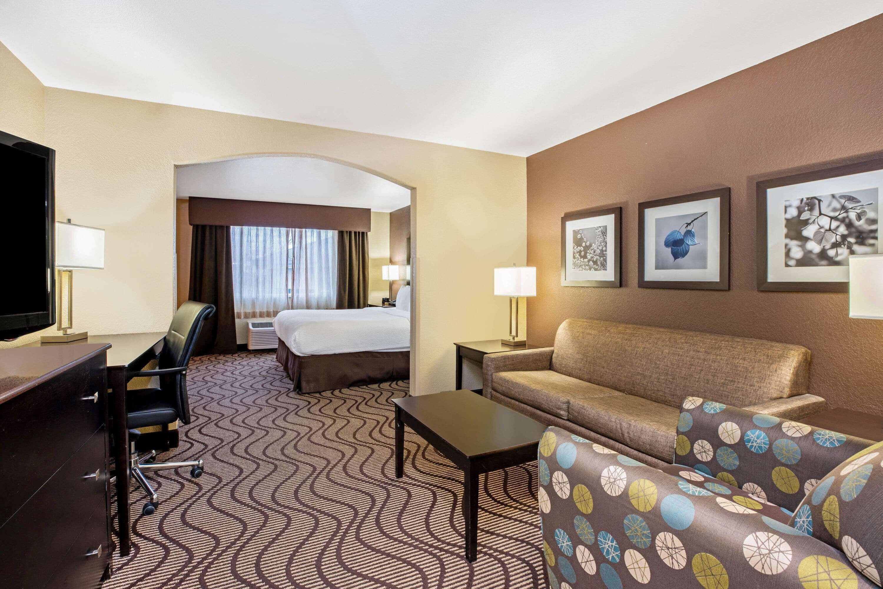 Hotelkamer met een bed, een bureau, een stoel, een bank en een salontafel. Er hangen drie ingekaderde foto’s aan de muur.
