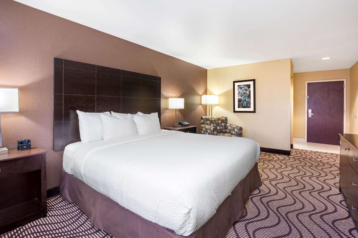 Een hotelkamer met een groot bed, een nachtkastje, een bureau, een stoel, een lamp en een deur.