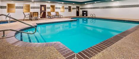 A swimming pool with a tiled edge, a lounge area with chairs, and a door in the background.