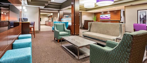 A hotel lobby with seating areas, a reception desk, and a television screen.