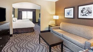 Camera d'albergo con un letto, un divano, una TV, una lampada e due quadri appesi al muro.