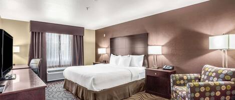 A hotel room with a large bed, a desk with a TV, a chair, and a patterned rug.