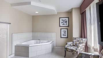 A modern bathroom with a large bathtub, two framed pictures on the wall, and a chair with a patterned cushion.