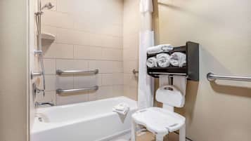 A bathroom with a white bathtub, a shower, a white toilet, and a shelf with towels.