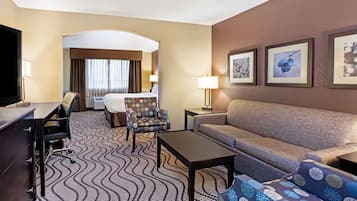 A hotel room with a bed, a sofa, a desk, a chair, and a TV.